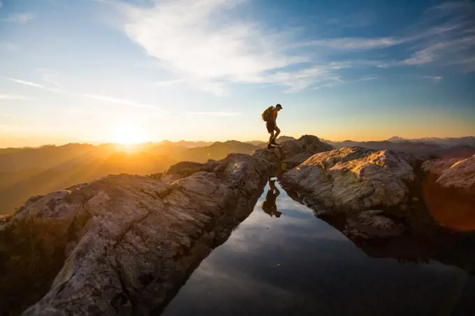 Backpacker hiking over rocky mountain terrain at sunset.