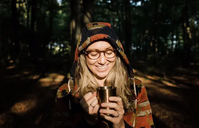 woman drinking hot drink happily in the forest