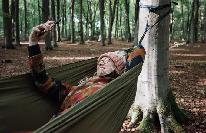 woman laying in a hammock in the forest taking a selfie