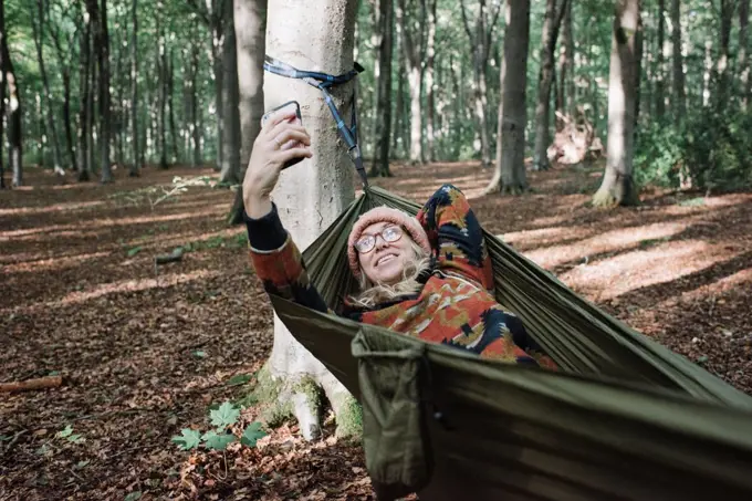 woman taking a selfie or FaceTime in the forest on a hammock