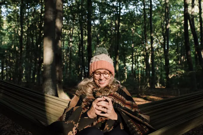 woman sat happily in a hammock in the forest having coffee