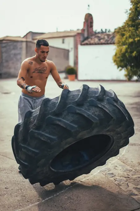 Boy training bodybuilding while pushing a tractor wheel