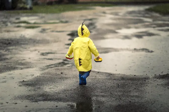 Toddler child in yellow raincoat and blue rain boots walking