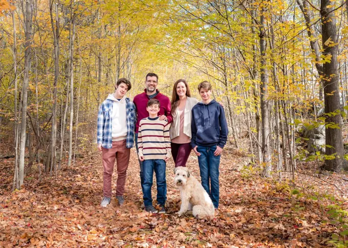 Portrait of family of five outside in wooded area on autumn day.