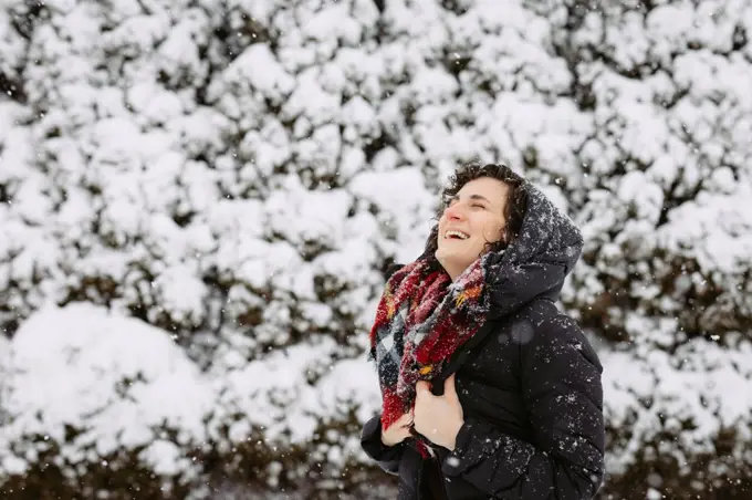 Woman in hood and red scarf smiling and laughing outside on snow