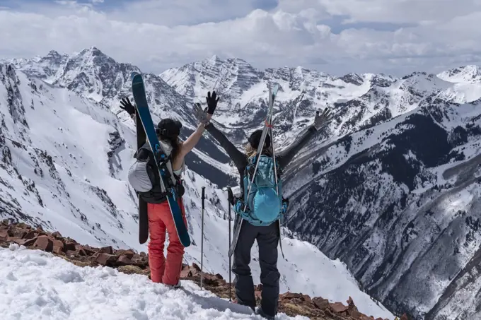 female friends with arms raised standing on snowcapped mountain