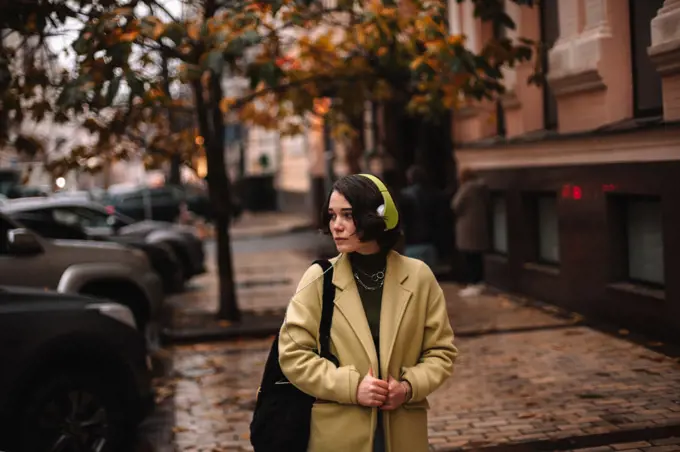 Thoughtful young woman listening music in headphones walking on street