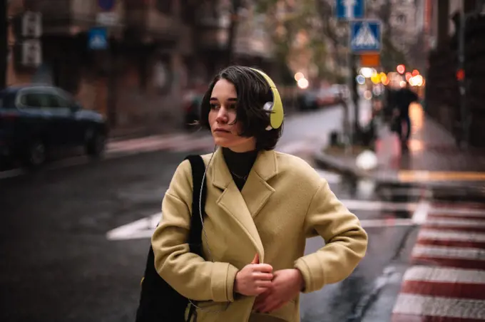 Thoughtful young woman in headphones walking on street in city