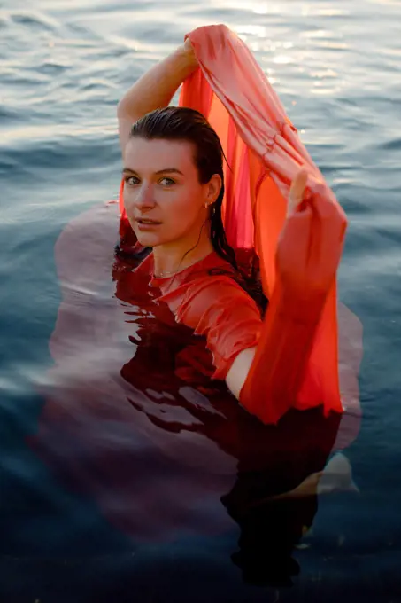 woman with blue eyes in a wet red dress in blue water