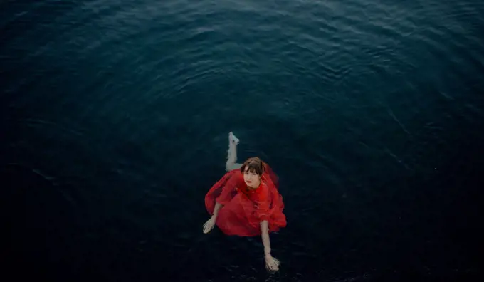 woman in wet red dress in dark blue water general shot from above