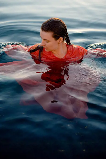 a woman in a wet red dress with wet hair swims in blue water