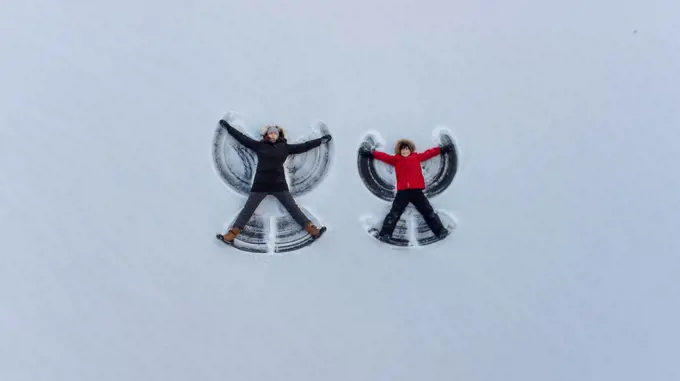 Overhead view of adult and child making snow angels together.