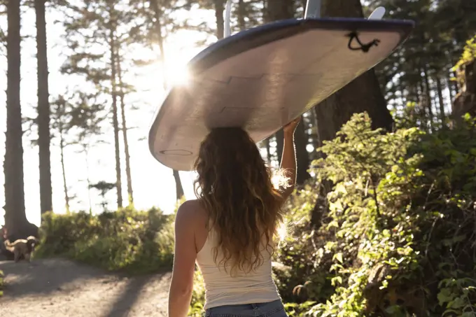 Woman carrying surfboard on her head down trail to the ocean