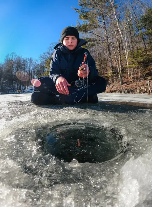 Teen boy ice fishing on a frozen lake on a cold winter day in Canada.