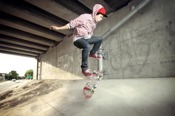 Young male skateboarding under overpass
