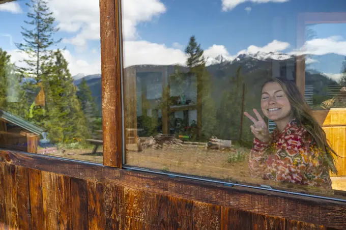 Female showing the peace sign through a mountain cabin window
