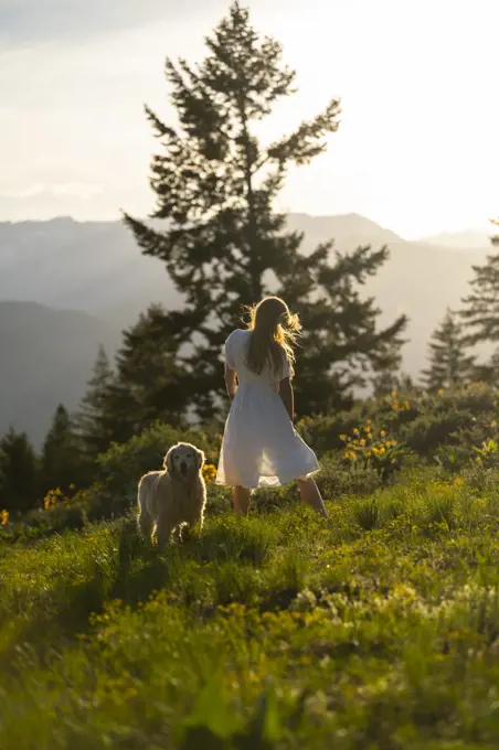 Female in a dress standing with her dog in the mountains