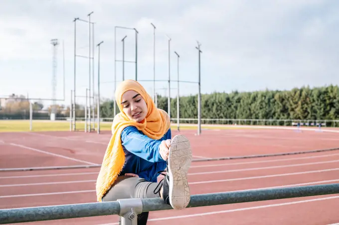 Arab woman stretching legs in stadium during workout