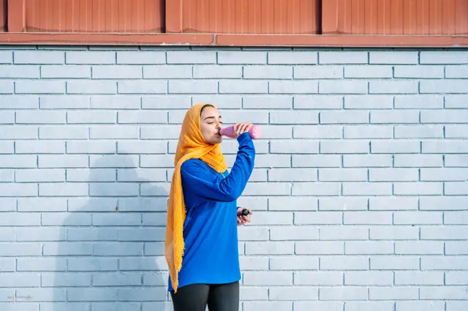 Arab woman drinking water near brick wall during training