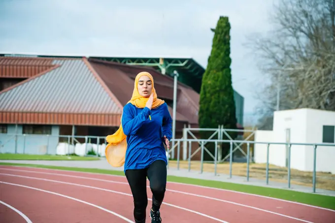 Ethnic woman in hijab and activewear running on racetrack
