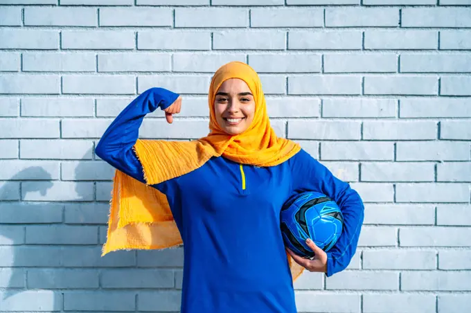Happy ethnic woman with soccer ball showing power gesture