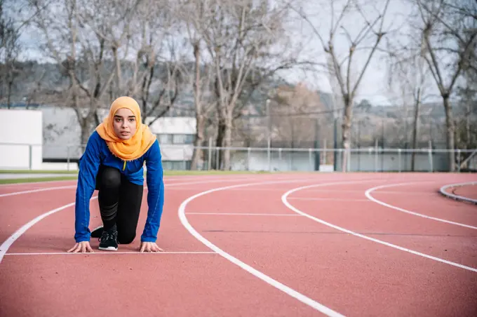 Serious ethnic woman in ready position on running track