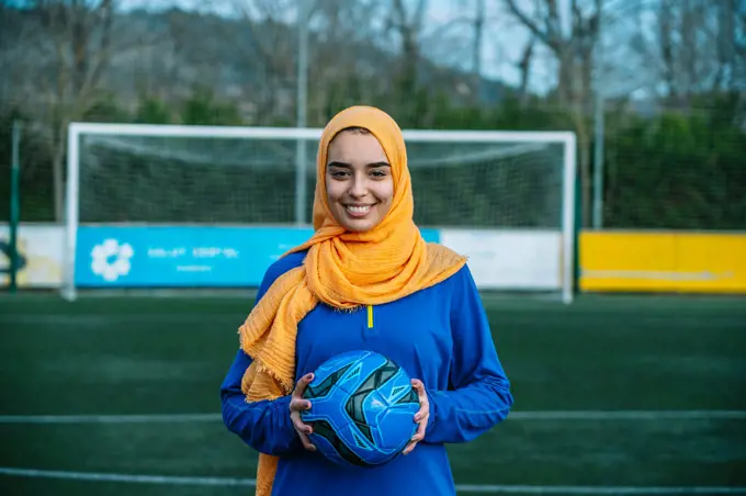 Smiling Arab female with ball on football field