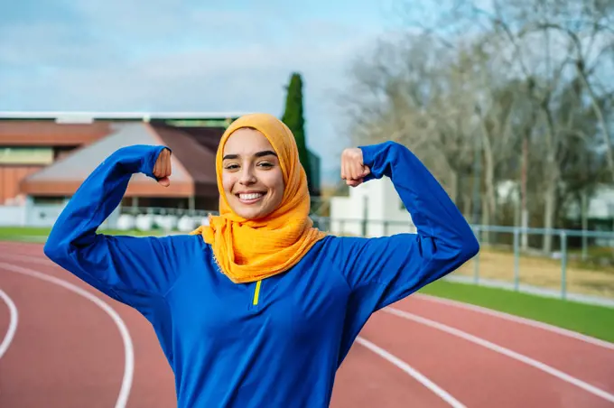 Cheerful Muslim ethnic woman showing hand muscles on track