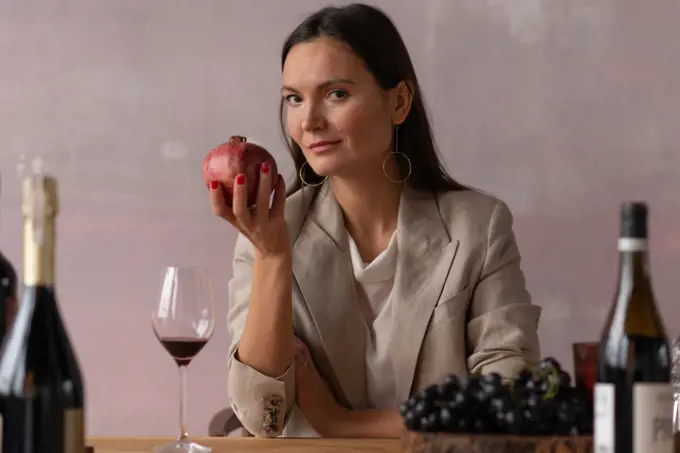 Sommelier woman among wine bottles holding pomegranate fruit