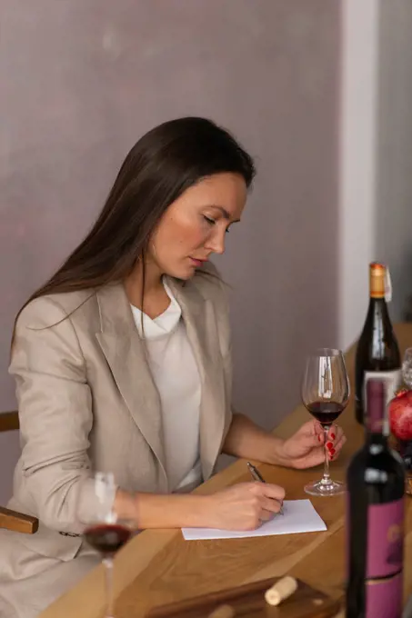 Beautiful brunette  female sommelier writing notes testing wine drink