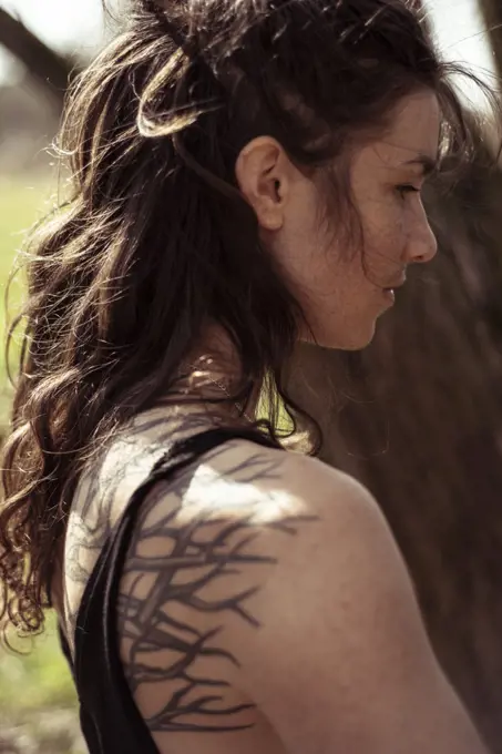 close portrait over shoulder of woman with tattoos outdoors in nature