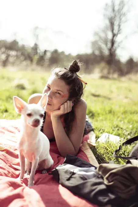 beautiful woman with small chihuahua lays in sun on grass in nature