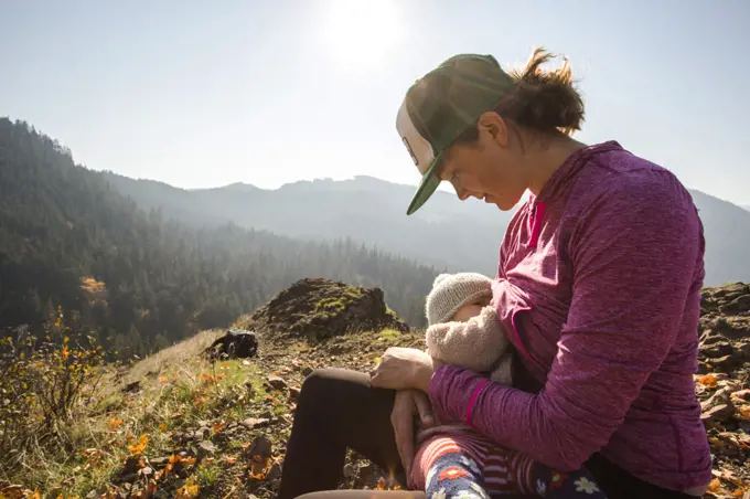 A young woman breast feeds an infant atop a mountain