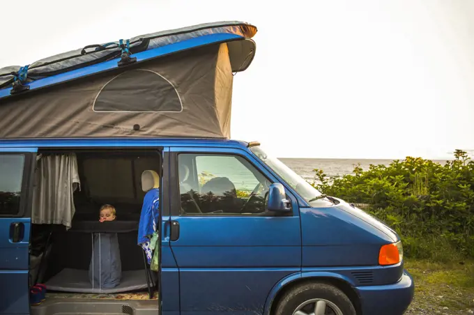 A small child in a pack-n-play inside a pop-top camper van by beach