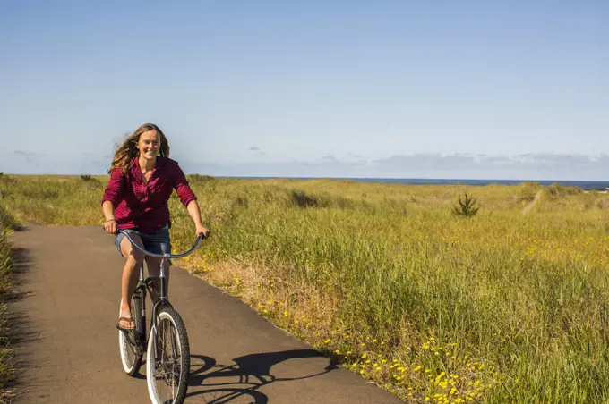 A young woman rides a beach cruiser bike on a paved path.