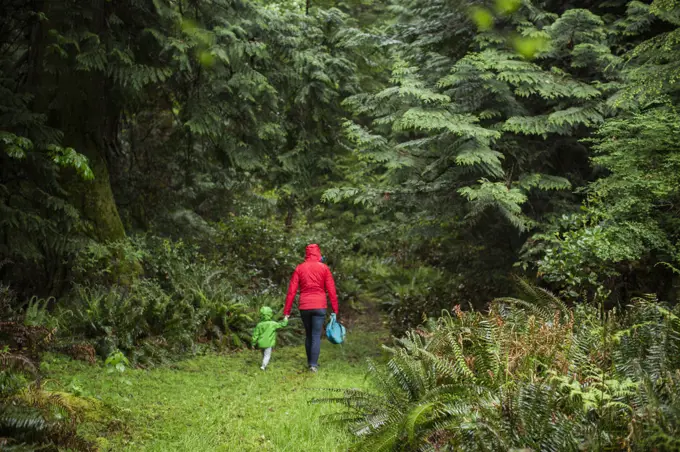 A woman in raincoat walks into forest with young child