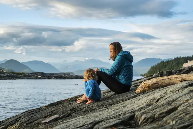 A mom sits with young child on a rock overlooking big bay