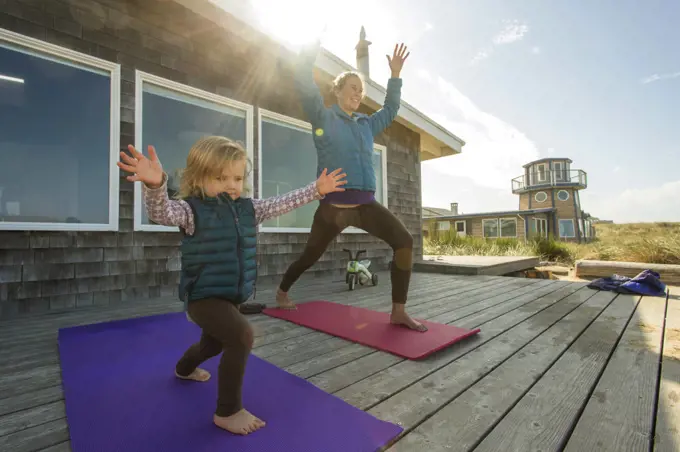 A young girl and her mother do yoga on a sunny deck