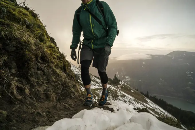 A man hikes up a mountain trail with snow and steep slope in distance