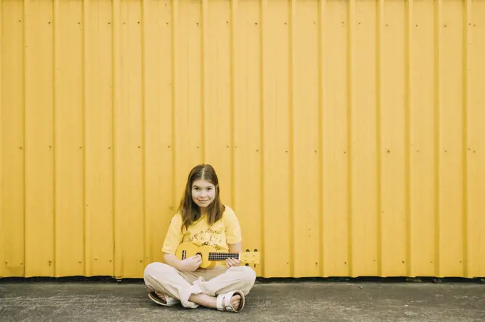 Young girl sitting outside playing a ukulele