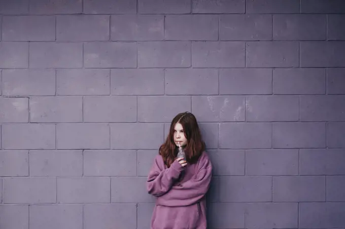 Girl standing against a purple wall drinking a smoothie