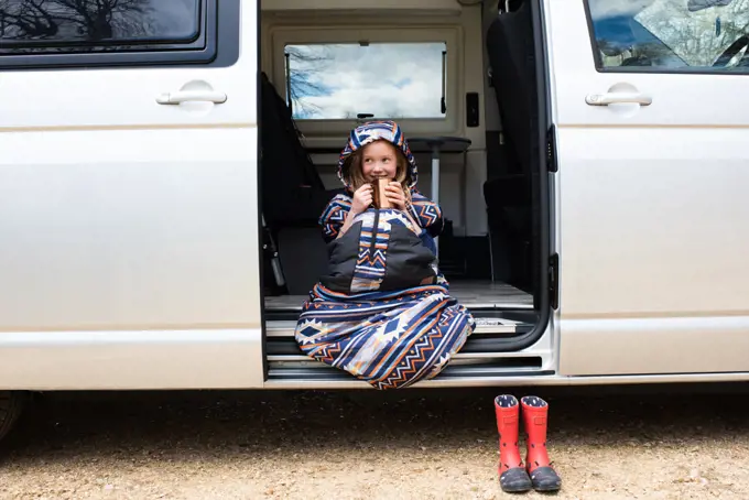 child enjoying a hot chocolate in the doorway of a campervan