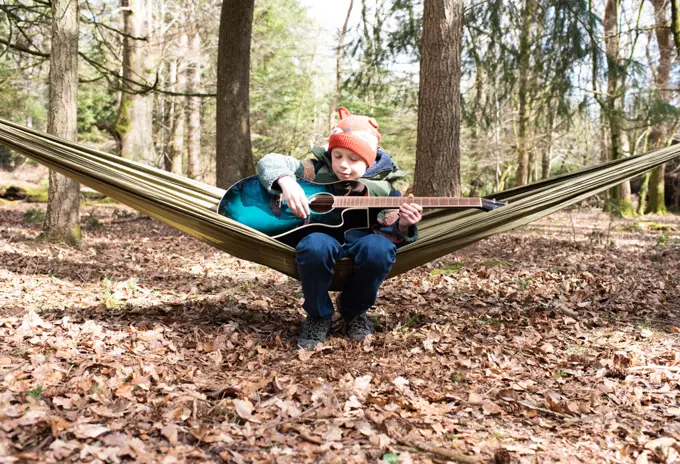 boy happily playing guitar in a hammock in the forest