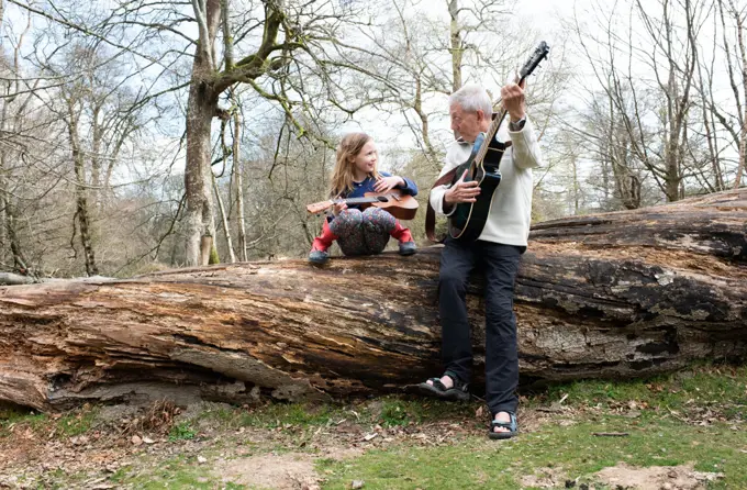 grandfather playing guitar with his granddaughter in the forest
