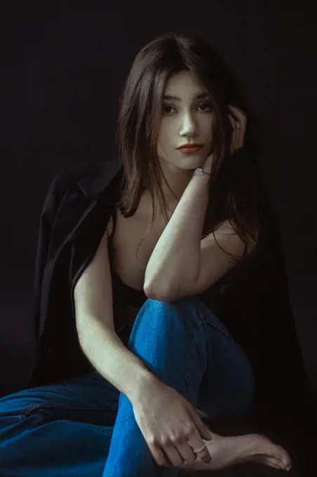 Young brunette in blue jeans and jacket on a black background