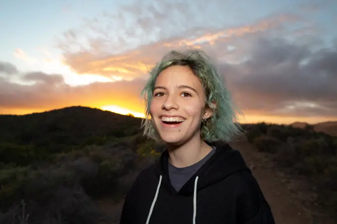 Teen Girl Laughing While On A Hiking Trail With A Sunset Behind Her
