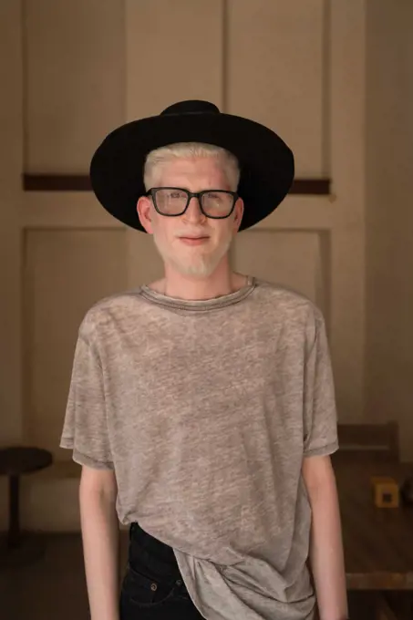 Albino man wearing hat and glasses standing by the wall portrait