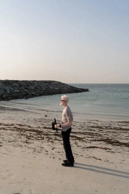 Albino man standing on the beach holding a hat