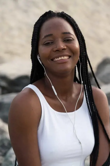 Woman with braids sitting at the beach wearing headphones