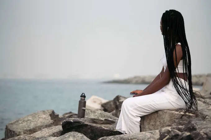 Woman with braids sitting at the beach listening to the music